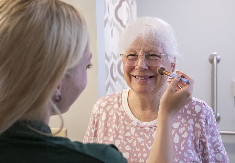 A smiling woman getting makeup applied.